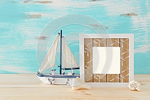 Nautical concept with empty photo frame and sail boat over wooden table. For photography montage