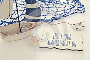 nautical concept image with white decorative sail boat and text over wooden board: ENJOY YOUR SUMMER VACATION.