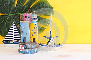 Nautical concept with sea life style objects as boat, driftwood beach houses, seashells and starfish over wooden table and yellow