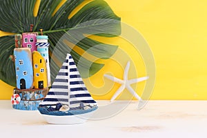 Nautical concept with sea life style objects as boat, driftwood beach houses, seashells and starfish over wooden table and yellow