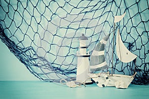 nautical concept with white decorative sail boat, lighthouse, seashells and fishnet over blue wooden table and background.