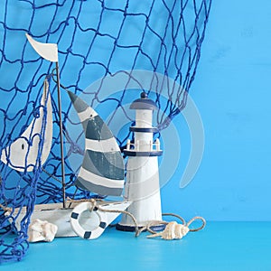 nautical concept with white decorative sail boat, lighthouse, seashells and fishnet over blue wooden table and background.