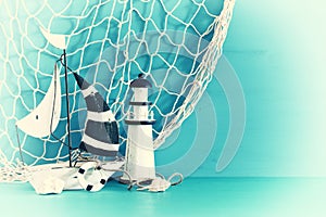 nautical concept with white decorative sail boat, lighthouse, seashells and fishnet over blue wooden table and background.