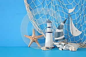 nautical concept with white decorative sail boat, lighthouse, starfish, seashells and fishnet over blue wooden table and backgroun