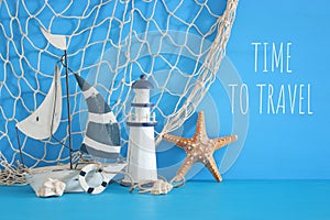 nautical concept with white decorative sail boat, lighthouse, starfish, seashells and fishnet over blue wooden table and backgroun