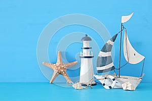 nautical concept with white decorative sail boat, lighthouse, starfish, seashells over blue wooden table and background.