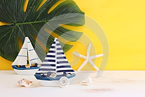 nautical concept with white decorative sail boat, seashells over wooden table and yellow background