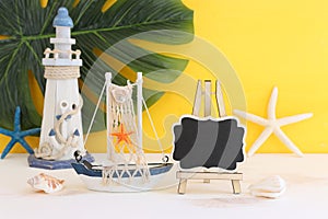 nautical concept with white decorative sail boat, seashells over wooden table and yellow background