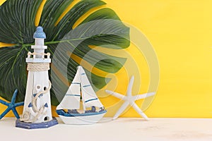 nautical concept with white decorative sail boat, seashells over wooden table and yellow background