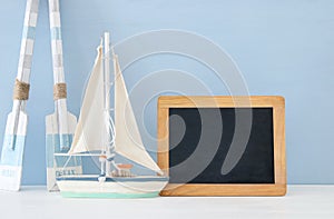 nautical concept with white decorative wooden oars and boat next to empty blackboard over blue background.