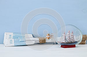 nautical concept with wooden oars and boat in the glass bottle over blue background.