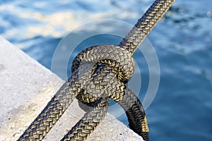 Nautical knot on a yacht rope against the background of water on the pier. Yacht tied with a rope in the seaport.