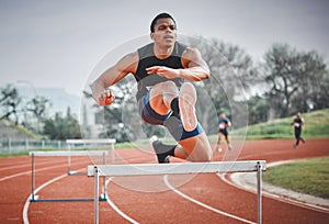 Navigating obstacles with ease. Full length shot of a handsome young male athlete practicing hurdles on an outdoor track