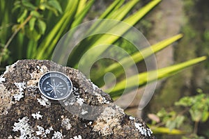 Navigation concept - Analogical compass laying on the rocky stone. Agave plant leaves in background