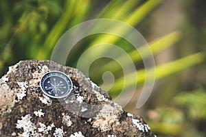 Navigation concept - Analogical compass laying on the rocky stone. Blurred agave plant leaves in background