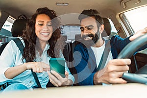 Navigation concept. Happy arab spouses driving car using smartphone and setting gps on phone