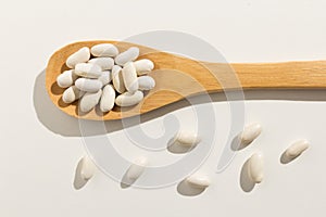 Navy Bean legume. Healthy grains on a wooden spoon. White background.