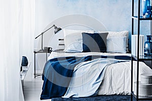 Navy blue blanket on bed in pastel bedroom interior with lamp on