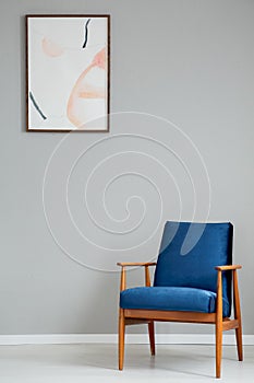 Navy blue wooden armchair in simple grey living room interior with poster on the wall