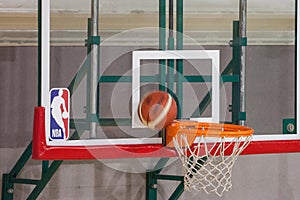 NBA logo on a backboard while a basketball is about to score on its ring.