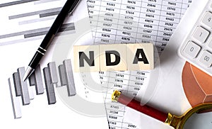 NDA text on wooden block on graph background with pen and magnifier