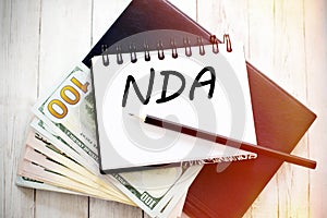 NDA text written on notebook with dollar bills and pencil. Financial concept