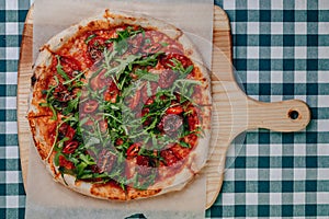 Neapolitan spicy pizza with ham, cheese, arugula, basil, tomatoes, pepperoni pepper sprayed with cheese on a wooden board on a