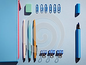Near blue pencil case lie pens, rubber, markers, and paper clips