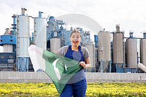 near suburban factory,cheerful female worker in overalls stands and holds flag of Pakistan in hands