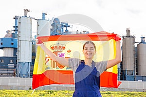 near suburban factory,cheerful female worker in overalls stands and holds Spanish flag in her hands