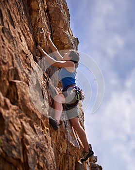 So near to her goal. A young woman reaching to clip a bolt while rock climbing.