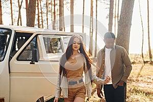 Near the white bus. Young couple is traveling in the forest at daytime together