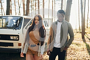 Near the white bus. Young couple is traveling in the forest at daytime together