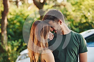 Near white colored car. Beautiful young couple have a good time in the forest at daytime