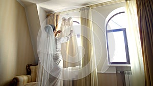 Near window, in room, white wedding dress hanging on the window eaves. the bride, a beautiful girl in a white peignoir