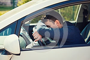 Nearly sleeping casual man keeps hand and head on the steering wheel being tired waiting in the traffic jam after work in the rush