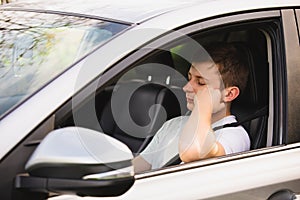 Nearly sleeping yound driver being tired waiting in the traffic jam after work in the rush hour. Exhausted young guy stop driving