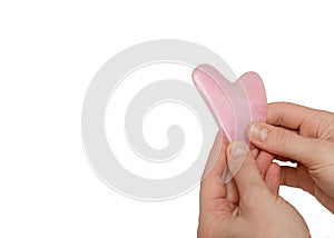 Neat female hands of a cosmetologist masseur hold a gouache scraper made of pink jade in the shape of a heart. Face body skin care