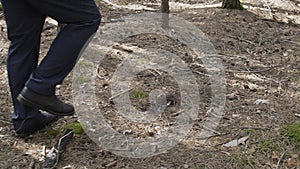 A neat man in a black jacket and shoes walks through the forest on the legs of a man