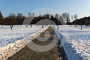A neat paved path cleared of snow and ice in a snowy city park