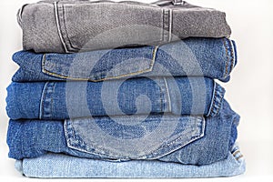 Neat stack of various shades of blue jeans on a white shelf. Clothes storage. Laundry and ironed denim clothes. Copy space for