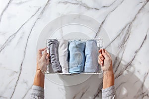 Neatly folded clothes and pyjamas in the metal mesh organizer basket on white marble table.
