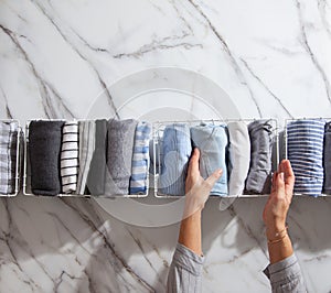 Neatly folded clothes and pyjamas in the metal mesh organizer basket on white marble table.