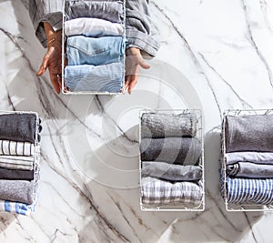 Neatly folded clothes and pyjamas in the metal mesh organizer basket on white marble table.