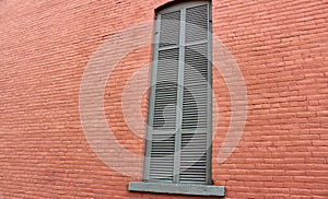 Old red and pink brick exterior wall of home with one long shuttered window