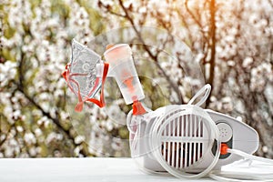 Nebulizer with a mask on the background of a blossoming tree. Spring exacerbation photo