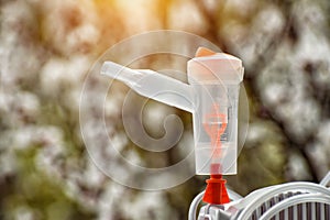 Nebulizer with a mask on the background of a blossoming tree. Spring exacerbation. Close up photo