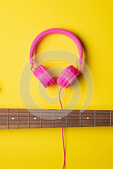 neck of a 5-string guitar placed horizontally and pink headsets on top of the neck