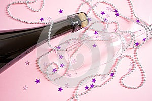 Neck of a bottle of champagne and a glass on a pastel pink background.