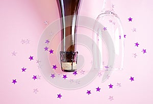 The neck of a bottle of champagne and a glass on a pastel pink background